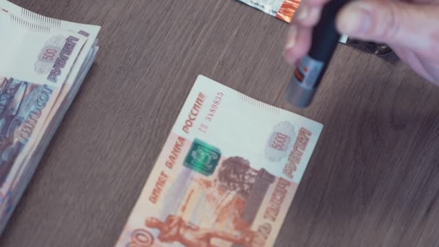 Mano-femenina-con-láser-para-comprobar-billetes-de-5-mil-rublos-en-la-mesa