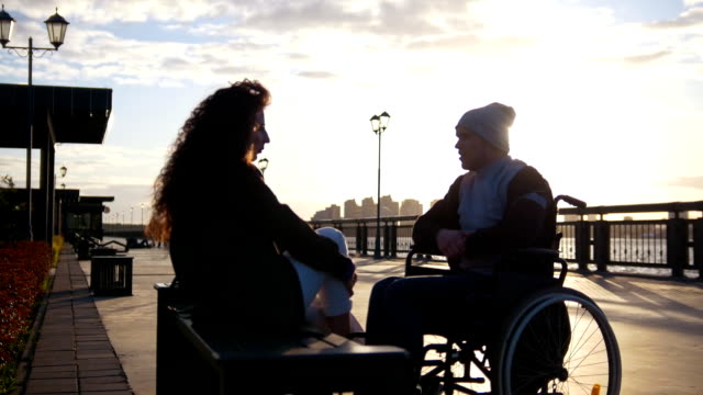 Glückliches-Paar---behinderten-jungen-Mann-im-Rollstuhl-mit-jungen-Frau,-die-zusammen-den-Sonnenuntergang-genießen