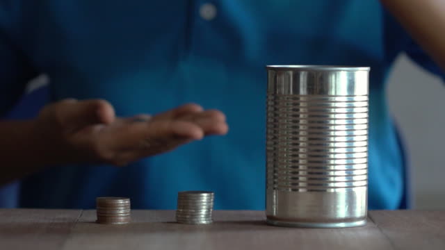Woman-drop-a-coin-into-a-old-can-on-table.