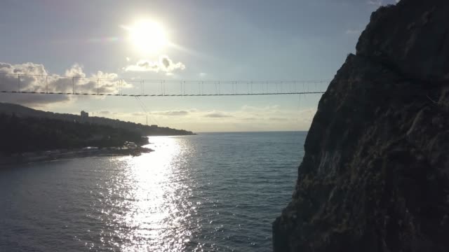 Luftaufnahme-der-Hängebrücke-zwischen-den-Felsen-über-dem-Meer-und-Gefahr-Wellen-und-Steinen