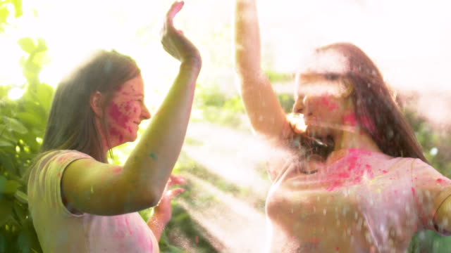 Ladies-spraying-colorful-powder-into-air-and-kissing-in-bright-cloud,-happiness