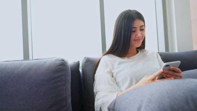 Asiatische-Frauen-im-Wohnzimmer-überprüfen-Smartphone-im-sozialen-Netzwerk.