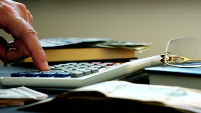 Hand-zählen-auf-einen-Rechner-und-Geld-auf-dem-Schreibtisch.