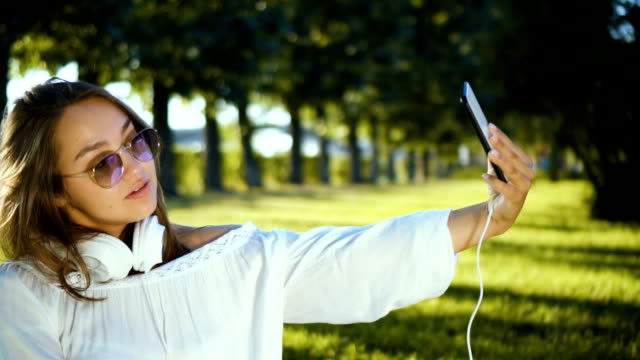 Hermosa-chica-teniendo-selfie-video-utilizando-smartphone-al-aire-libre-chica-compartir-fotografía-en-las-redes-sociales-con-el-teléfono-móvil