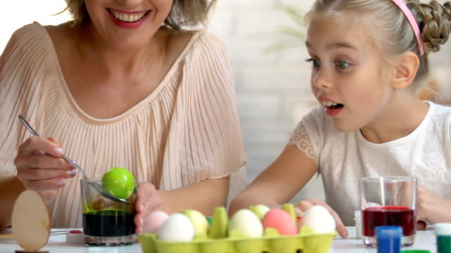 Little-kid-excitedly-watching-mom-dying-egg-in-green-food-coloring,-Easter-decor