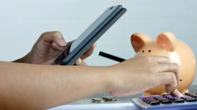Eine-Frau-ist-Notizen-machen-und-per-Smartphone-mit-einem-Rückgang-von-Geld-in-ein-Sparschwein