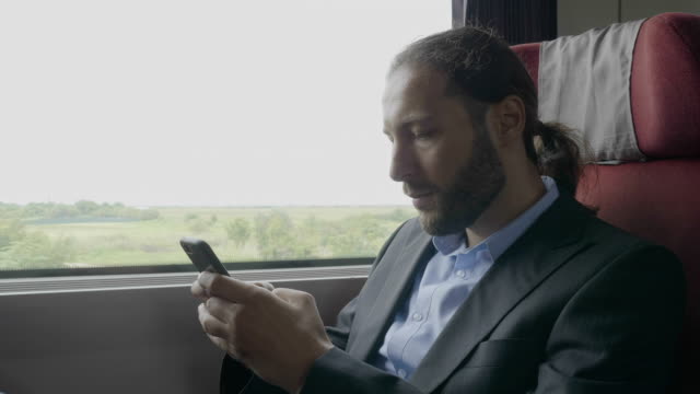 Young-entrepreneur-man-commuter-on-train-sitting-next-the-window-using-smartphone-on-his-way-to-office