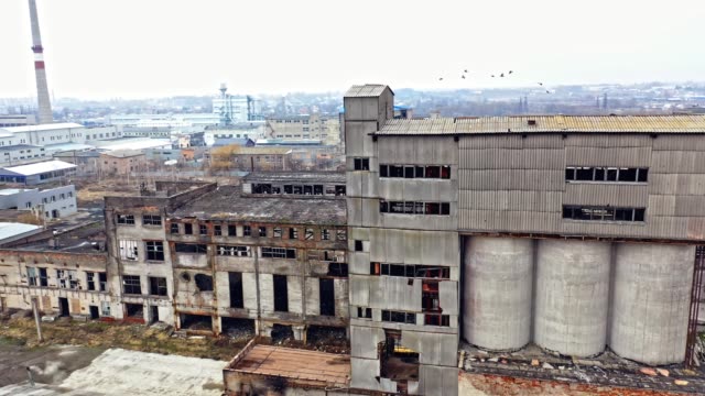 A-huge-state-owned-factory-with-gray-walls-and-broken-glasses-in-the-windows-on-the-background-of-city-buildings.-Industrial-zone.