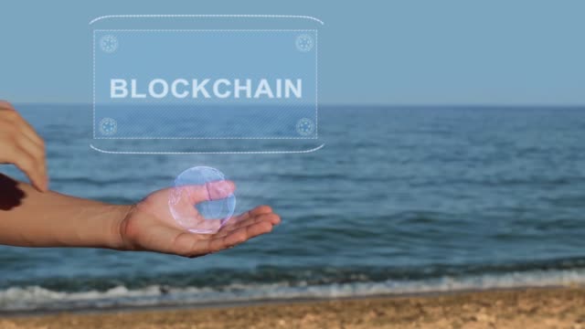 Männliche-Hände-am-Strand-halten-ein-konzeptionelles-Hologramm-mit-dem-Text-Blockchain
