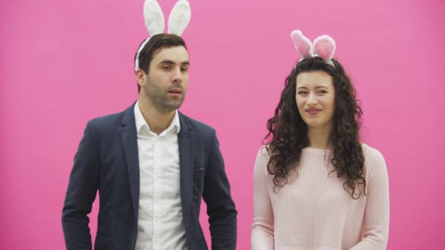 Young-couple-standing-standing-on-pink-background.-During-this-time,-they-are-dressed-in-rabble-ears.-Looking-at-each-other-smiles-sincerely