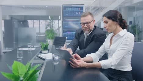 En-la-sala-de-reuniones-ejecutivo-femenino-muestra-tableta-digital-de-ordenador-a-inversor-masculino,-que-discutir-estadísticas-y-el-potencial-de-inversión-de-empresas.-Oficina-Corporativa-ocupada-con-empresarios-que-trabajan