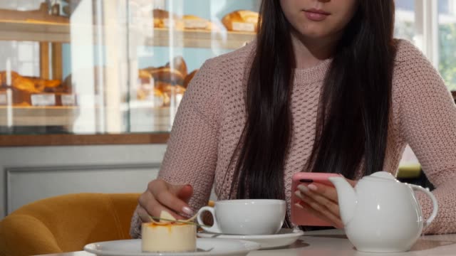 Mujer-irreconocible-usando-teléfono-inteligente-mientras-bebe-té-caliente-en-la-cafetería