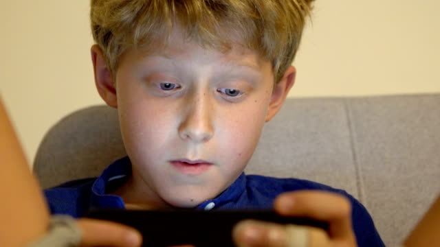4K-boy-sitting-on-couch-playing-his-smartphone
