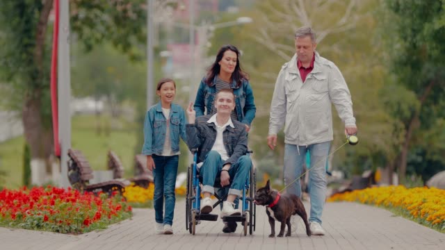 Happy-family-spends-the-day-together-for-a-walk-in-the-park.-Young-man-with-disabilities-walks-with-his-parents,-sister-and-dog.