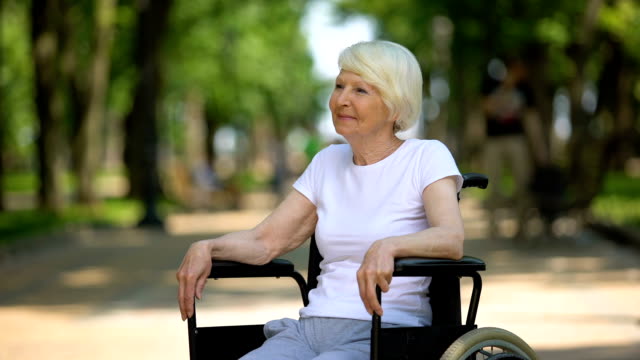 Lächelnde-alte-Frau-im-Rollstuhl-genießen-sonnigen-Tag-im-Krankenhauspark,-Erholung