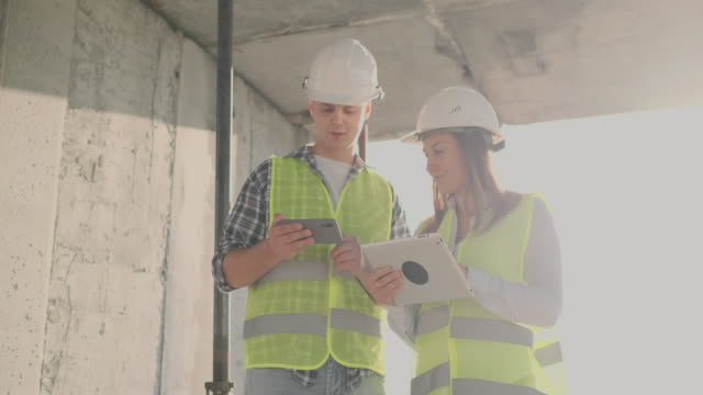 Engineers-designers-stand-on-the-roof-of-the-building-under-construction-and-discuss-the-plan-and-the-progress-of-construction-using-a-tablet-and-mobile-phone