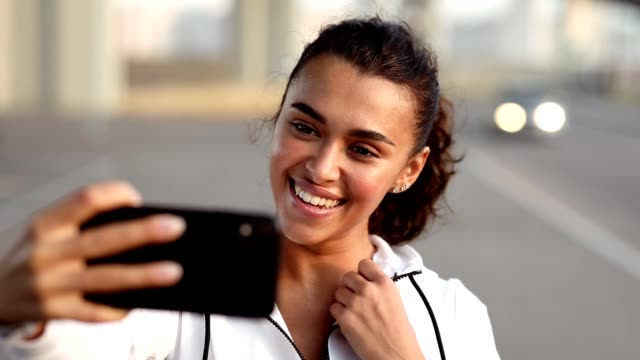 Young-woman-in-sportswear-taking-selfie-with-her-mobile-phone.-Happy-female-relaxing-after-workout.