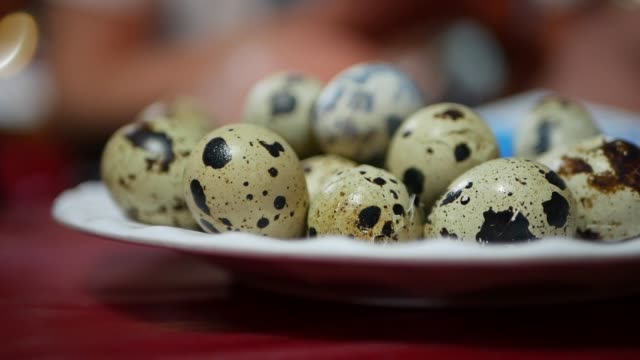 Female-hand-takes-small-quail-egg-from-the-plate-on-table-at-night-asian-market.-Closeup-of-fresh-quail-eggs