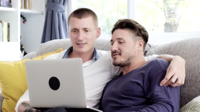 Schwules-Paar-entspannen-auf-der-Couch-mit-Laptop-Computer.-Verwirrender-Zustand.