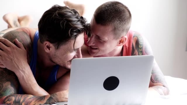 Schwules-Paar-im-Bett-mit-Laptop-Computer.-Kleine-süße-Rede.