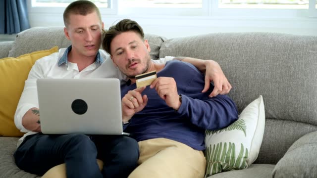 Pareja-gay-relajándose-en-el-sofá-usando-la-computadora-portátil.-Intente-comprobar-el-error-en-el-ordenador-portátil.