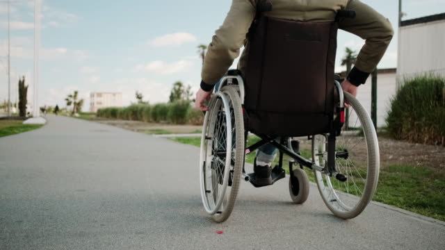 Hombre-discapacitado-en-silla-de-ruedas-se-está-moviendo-sobre-la-calle-de-verano,-vista-trasera