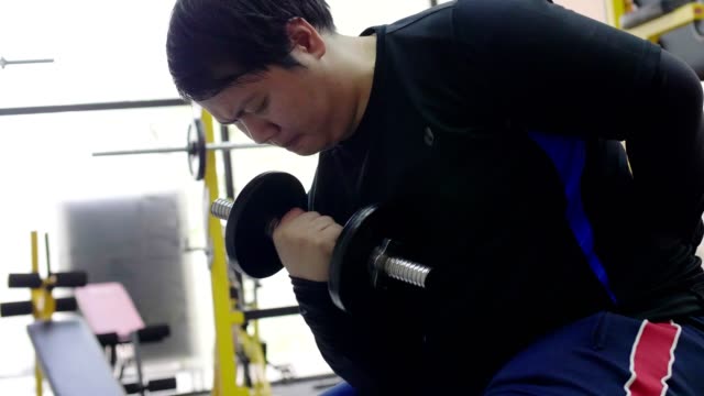 Asian-man-trying-to-exercise-with-dumbbell-in-fitness-gym,-Healthy-lifestyle,-weight-loss-desire