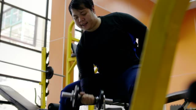 Asian-man-trying-to-exercise-with-dumbbell-in-fitness-gym,-Healthy-lifestyle,-weight-loss-desire