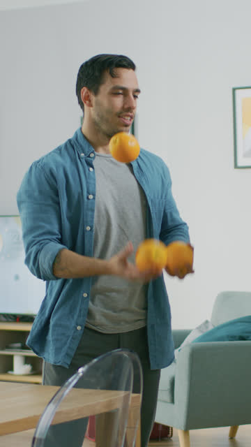Handsome-Young-Man-Has-Fun-in-the-Living-Room-Juggling-with-Oranges,-Training-for-his-Big-Perfromance.-Video-Footage-with-Vertical-Screen-Orientation-9:16