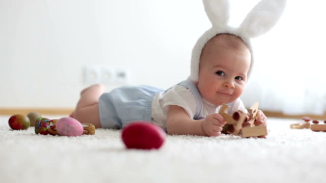 Lindo-niño-pequeño,-niño,-en-la-sala-de-estar-soleada-jugando-con-el-conejo-de-chocolate-de-Pascua-y-huevos-de-Pascua-coloridos