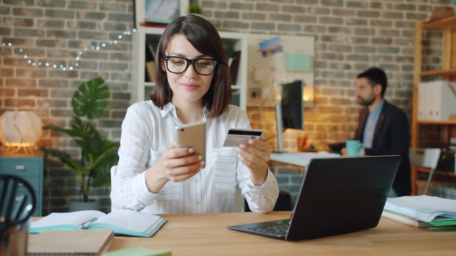 Young-woman-making-online-payment-with-credit-card-and-smartphone-at-work