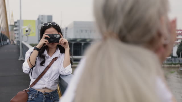Asian-lesbian-couples-enjoying-traveling-using-film-camera-taking-a-photo.-Two-beautiful-young-women-having-fun-in-vacation-time.