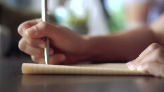 4K-video-copy-space-of-man-hand-writing-down-in-white-notebook-with-bokeh-light-in-cafe-background.
