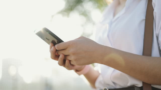 Nahhände-asiatische-Geschäftsfrau-in-einem-weißen-Hemd-verwendet-ein-Smartphone-SMS-Teilen-von-Nachrichten-auf-Social-Media,-während-außerhalb-des-Morgens-in-einem-öffentlichen-Park.
