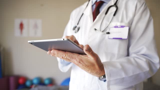 Close-up-of-male-doctors-hands-browsing-on-digital-tablet-in-consultation-room