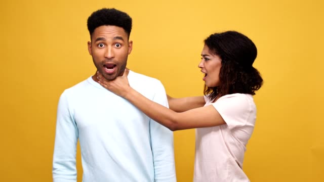 Violent-young-african-woman-strangling-her-boyfriend-isolated-over-yellow-background