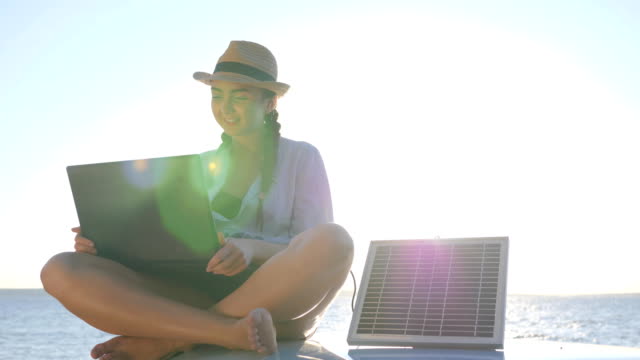 Reise,-junge-Frau-sitzt-auf-dem-Auto-Dach-mit-Notebook-und-Solar-Panel-auf-Hintergrund-Ozeanküste-im-Gegenlicht