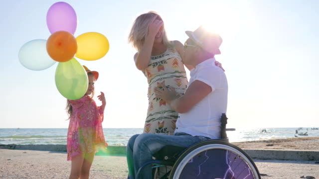 little-girl-listens-mother-and-father-with-handicap-in-wheel-chair-at-beach-in-summer-tim