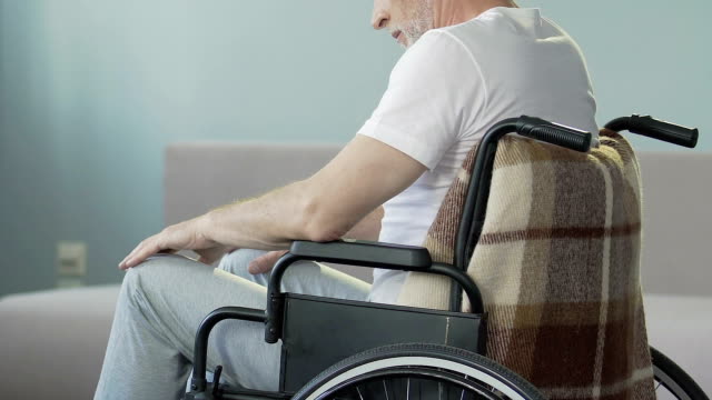 Hombre-anciano-sentado-en-silla-de-ruedas-mirando-las-piernas-y-colgantes,-pierde-capacidad-de-caminar