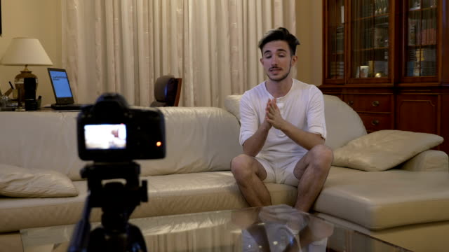 Young-social-media-influencer-shooting-a-new-episode-on-his-video-blog-with-a-camera-at-home-on-couch