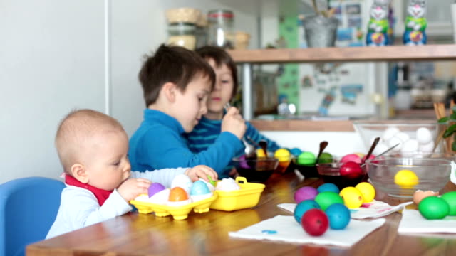 Three-children,-brothers,-coloring-and-painting-easter-eggs-at-home-in-kitchen-for-the-holiday