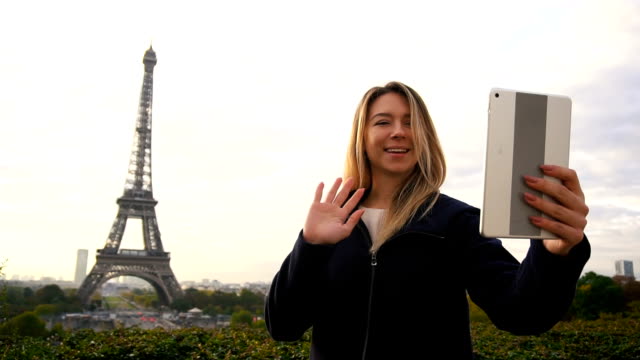 Cheerful-woman-making-video-call-by-tablet-with-Eiffel-Tower-background-in-slow-motion