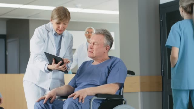 En-el-Hospital-femenino-médico-muestra-Tablet-PC-al-paciente-mayor,-explicando-su-condición.-Moderno-Hospital-con-la-mejor-atención-posible.