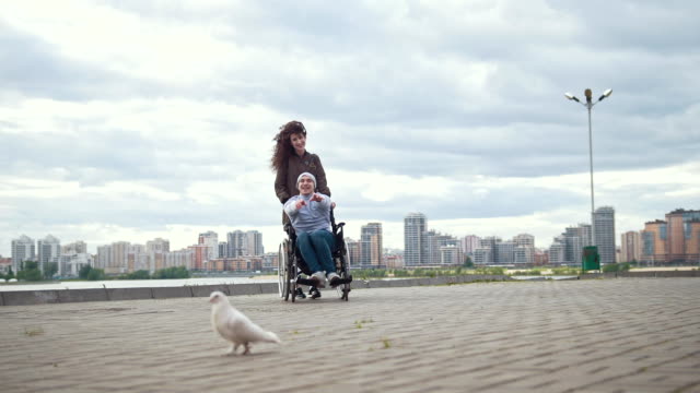 Hombre-discapacitado-en-silla-de-ruedas-con-mujer-joven-jugando-con-una-paloma