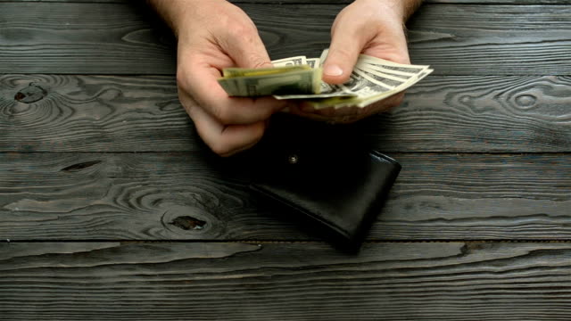 Man's-hands-count-the-US-dollars-and-cents,-banknotes-and-coins-from-a-black-leather-purse-over-a-dark-wooden-background.