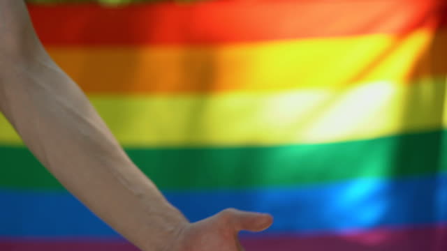 Homosexual-male-putting-wedding-ring-on-partner,-lgbt-flag-background,-equality