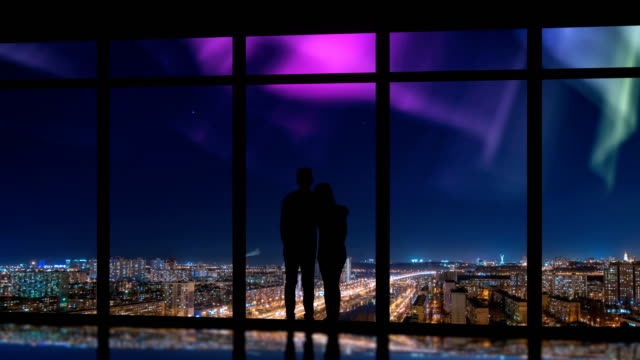The-couple-standing-near-windows-on-the-night-city-background.-time-lapse