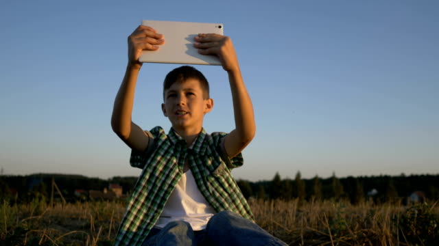 muchacho-hablando-por-video-llamada-en-tablet-sentado-en-el-campo-al-atardecer