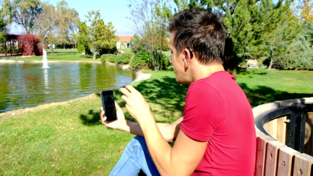 Young-deaf-boy-communicating-with-sign-language--at-smart-phone--in-park