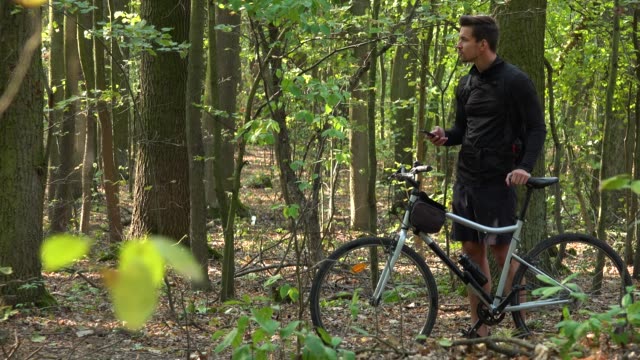 Ein-Radfahrer-steht-mit-einem-Fahrrad-in-einem-Wald-und-arbeitet-auf-einem-Smartphone